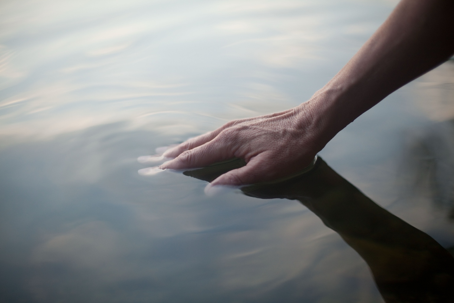 Eine Hand berührt die Oberfläche eines stillen Sees
